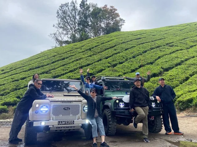 Group posing around two Land Rovers in a tea plantation